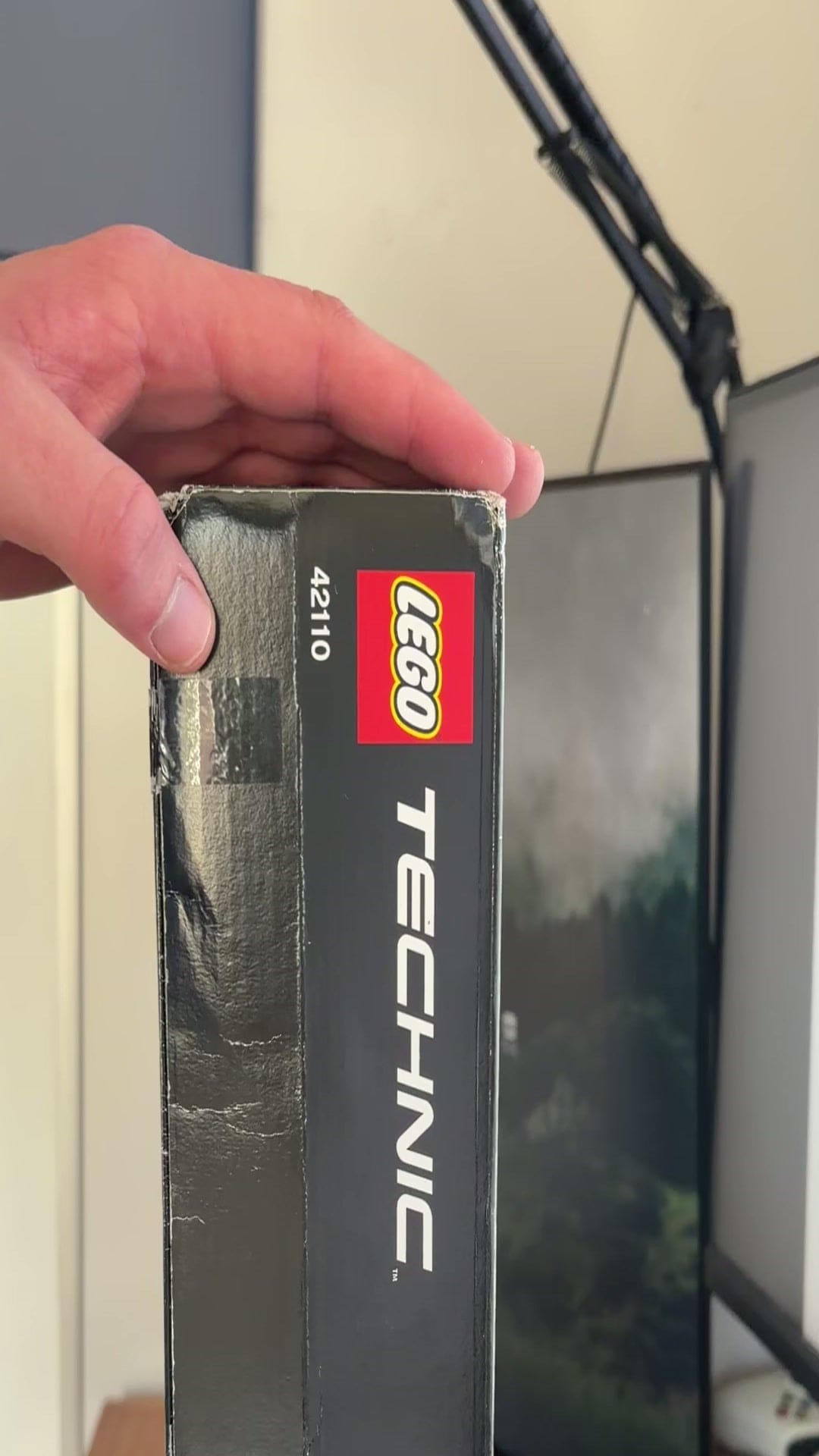 A hand holding a sealed LEGO box, seal side up